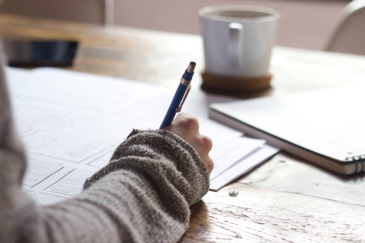 Hand writing notes beside a laptop