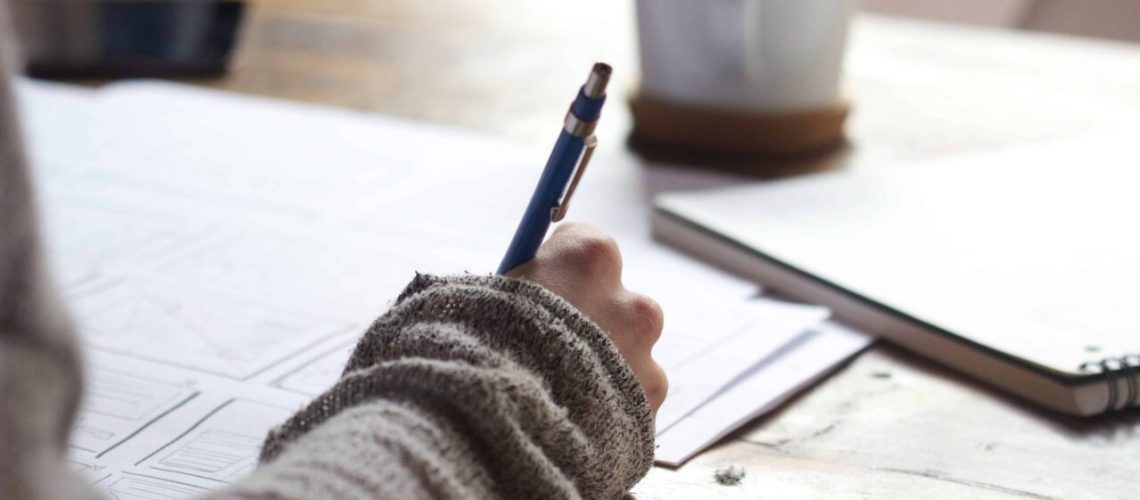 Hand writing notes beside a laptop